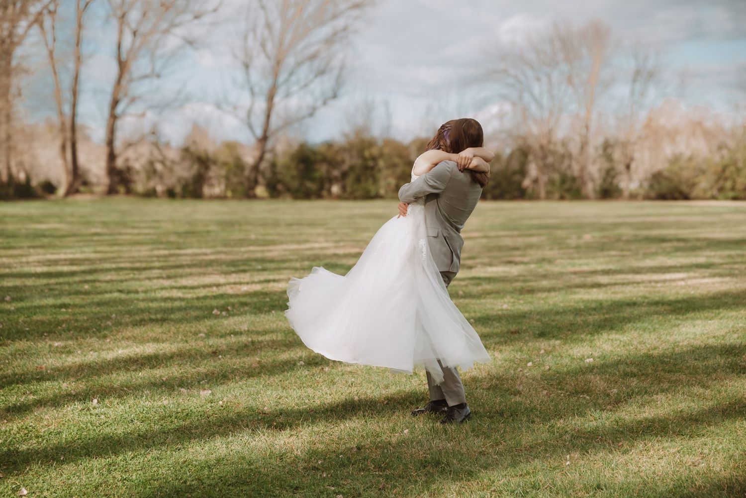 A couple dances together outdoors on a grassy lawn during their rustic wedding celebration.