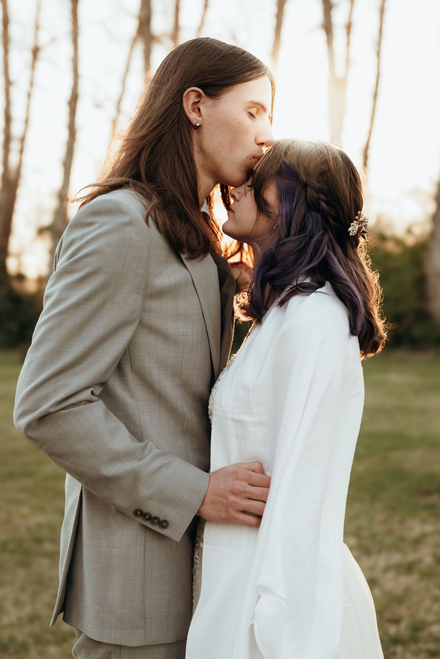 A couple shares an intimate moment at sunset in an outdoor wedding setting.
