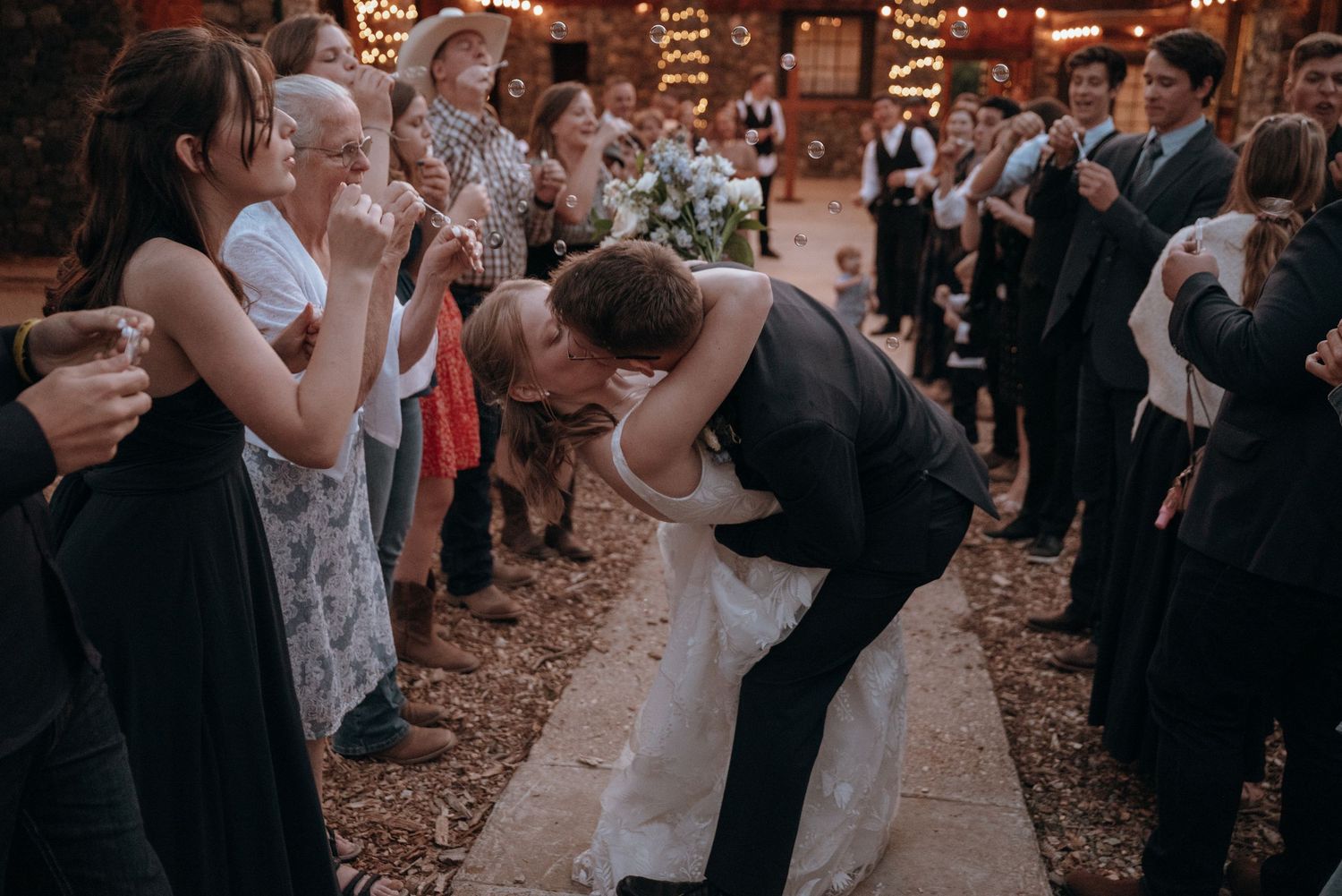 Wedding guests celebrate during an evening outdoor reception under warm lighting.