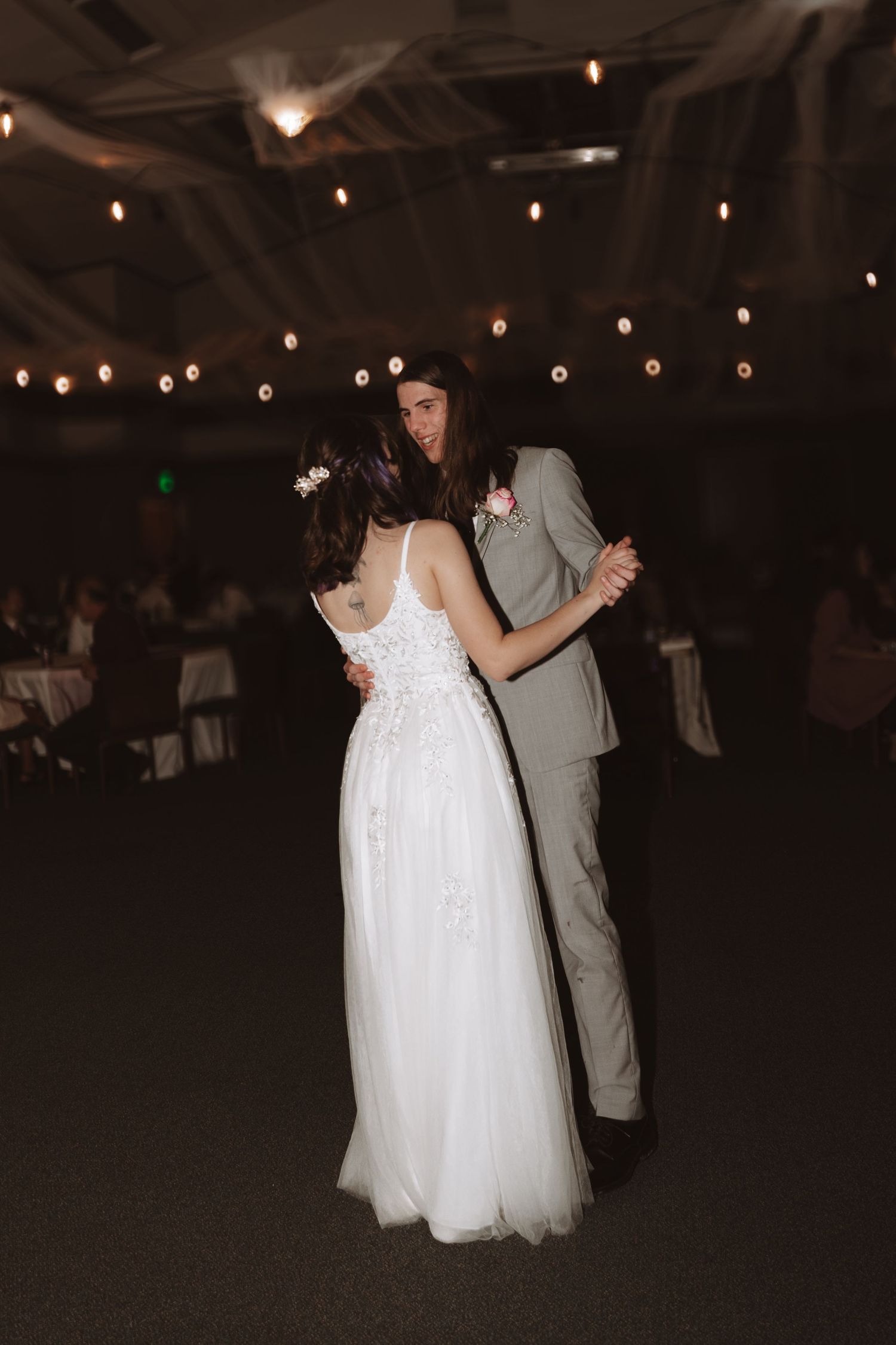 A couple slow dances under twinkling string lights at their evening wedding reception.