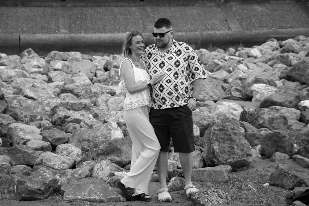 A black and white capture of a couple sharing a romantic moment among coastal rocks.
