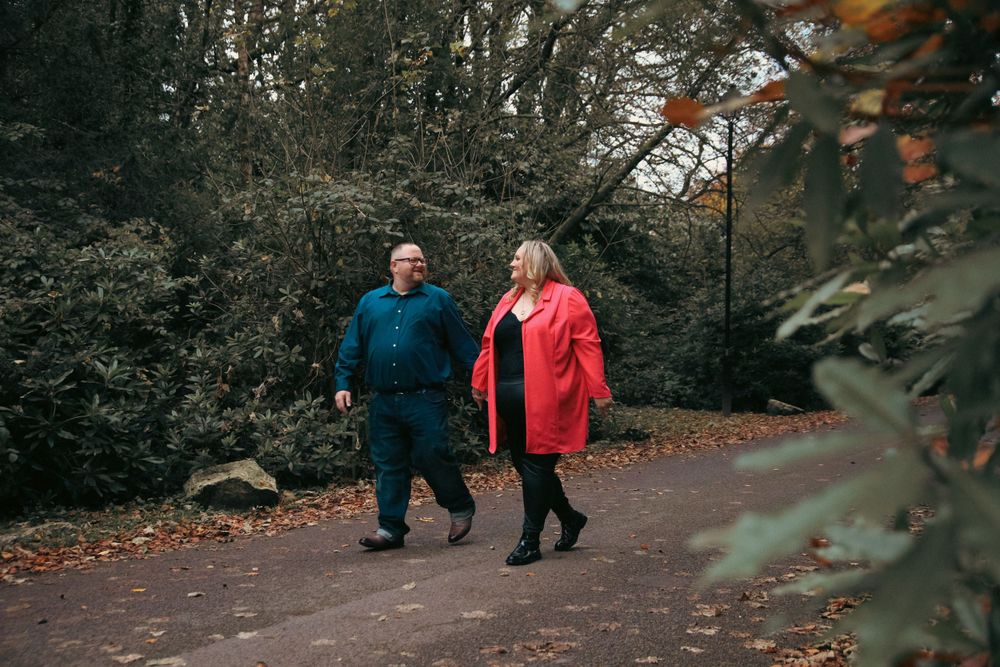 A couple in colorful winter coats takes an autumn stroll along a wooded path.
