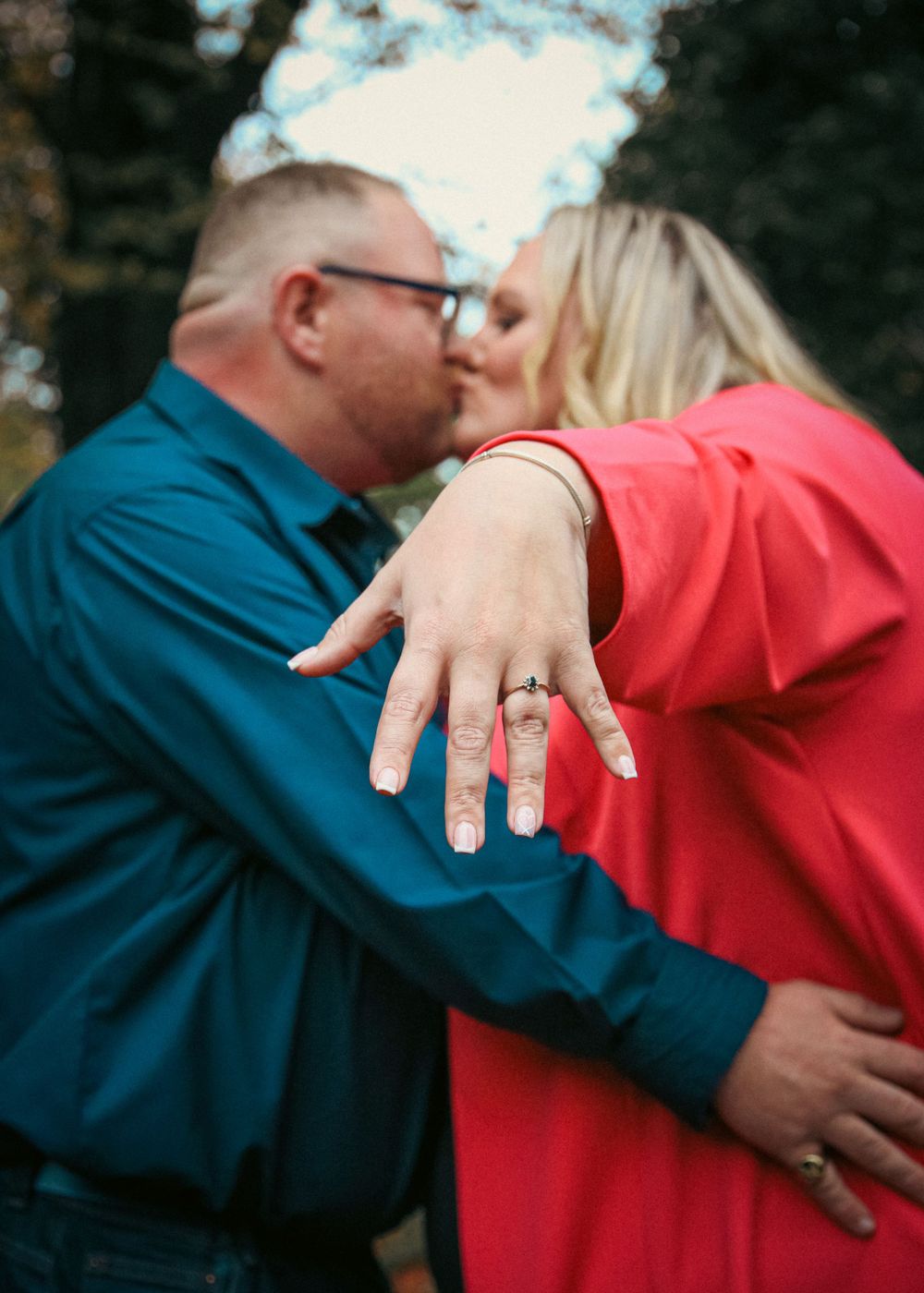 Engaged couple showing off ring while sharing romantic moment outdoors.