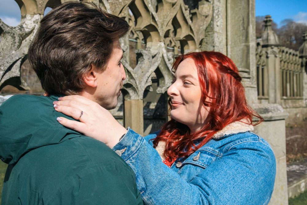 Happy couple in casual winter attire sharing an intimate moment outside historic gothic architecture.