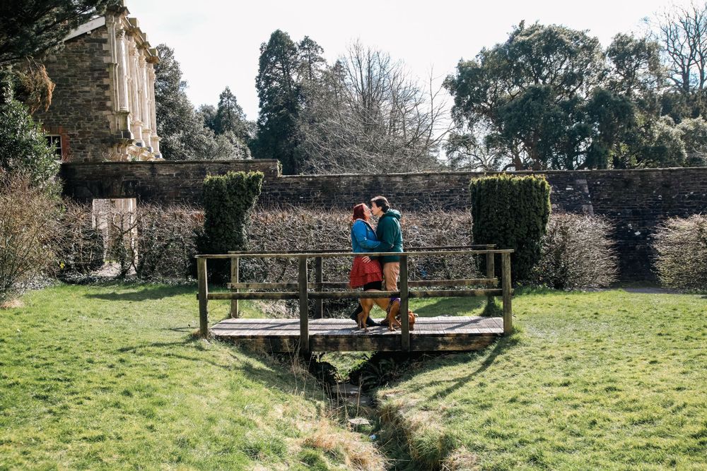 A tranquil figure rests on a wooden bridge spanning a small stream in a peaceful garden setting.