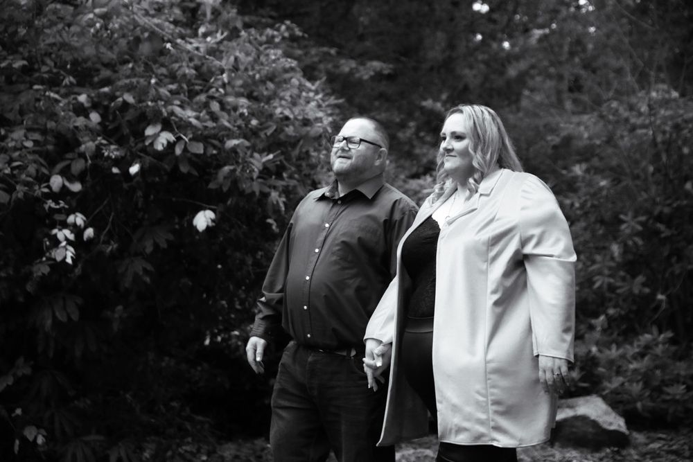 A candid black and white photograph of two people enjoying a moment in a garden setting.