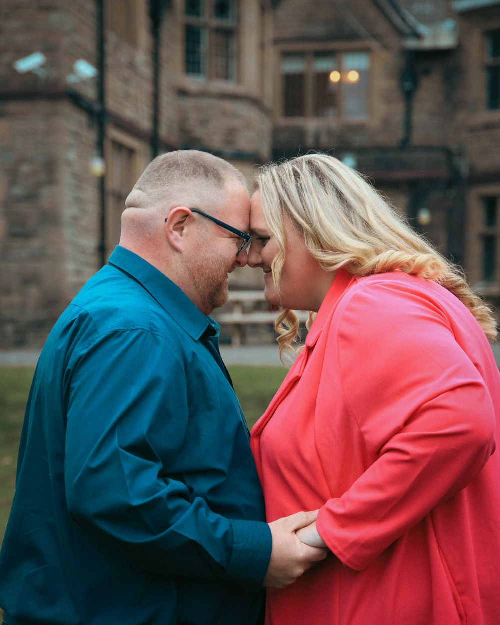 Intimate moment between couple in contrasting blue and coral outfits outside historic building.