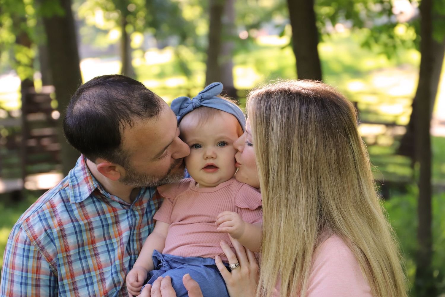 Parents kissing 1-year-old daughter on the cheek