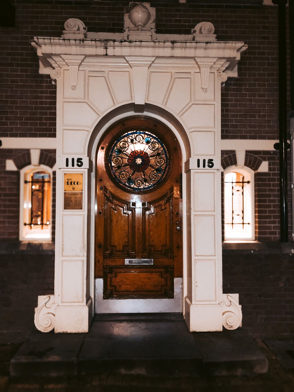 Row of elegant white archways with ornate wooden doors illuminated at night.