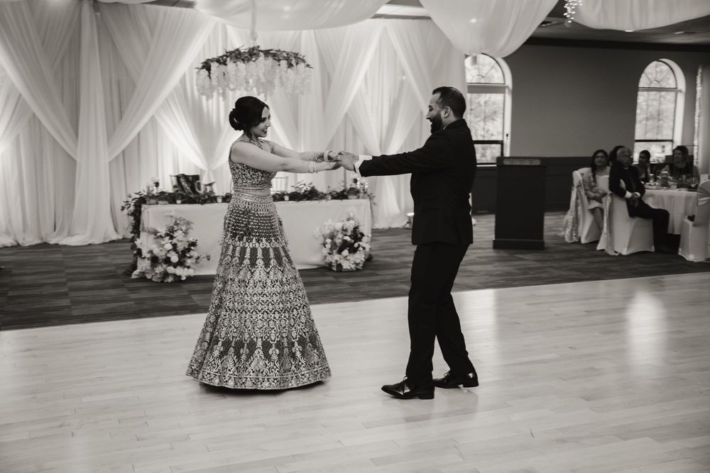 A couple performs a traditional dance in a beautifully decorated ballroom with white drapes and elegant decor.
