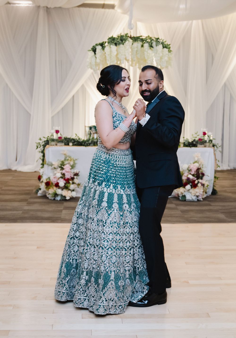 Dance moment in decorated reception space with white draping and floral arch.