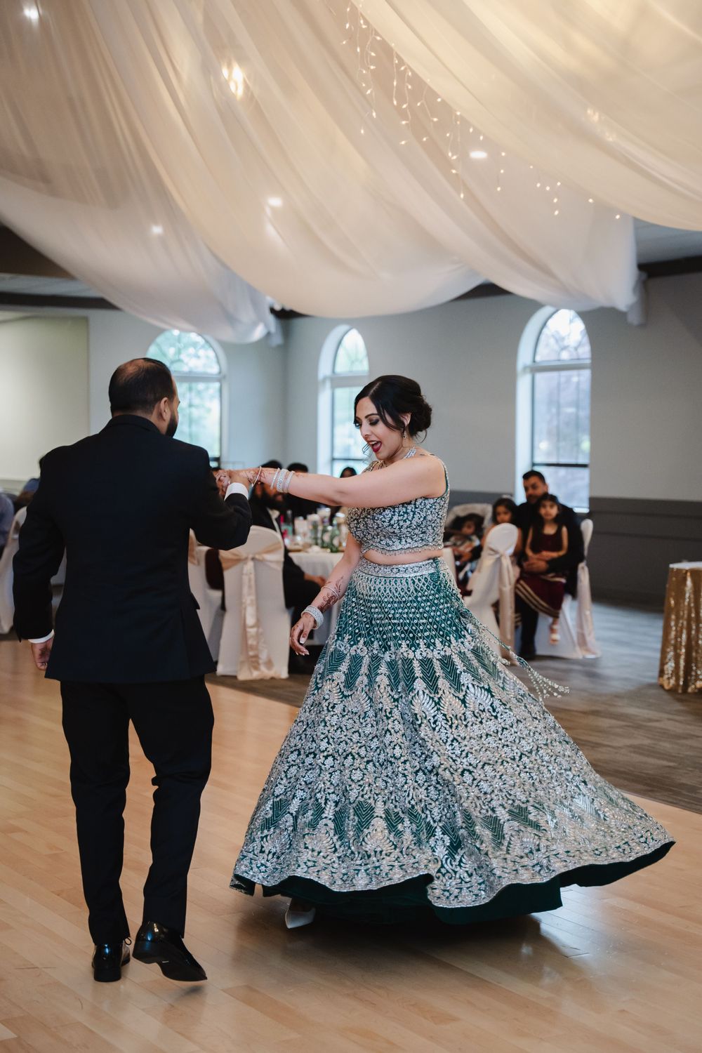 Dancers perform in an ornate green and white lehenga dress under draped fabric and twinkling lights.