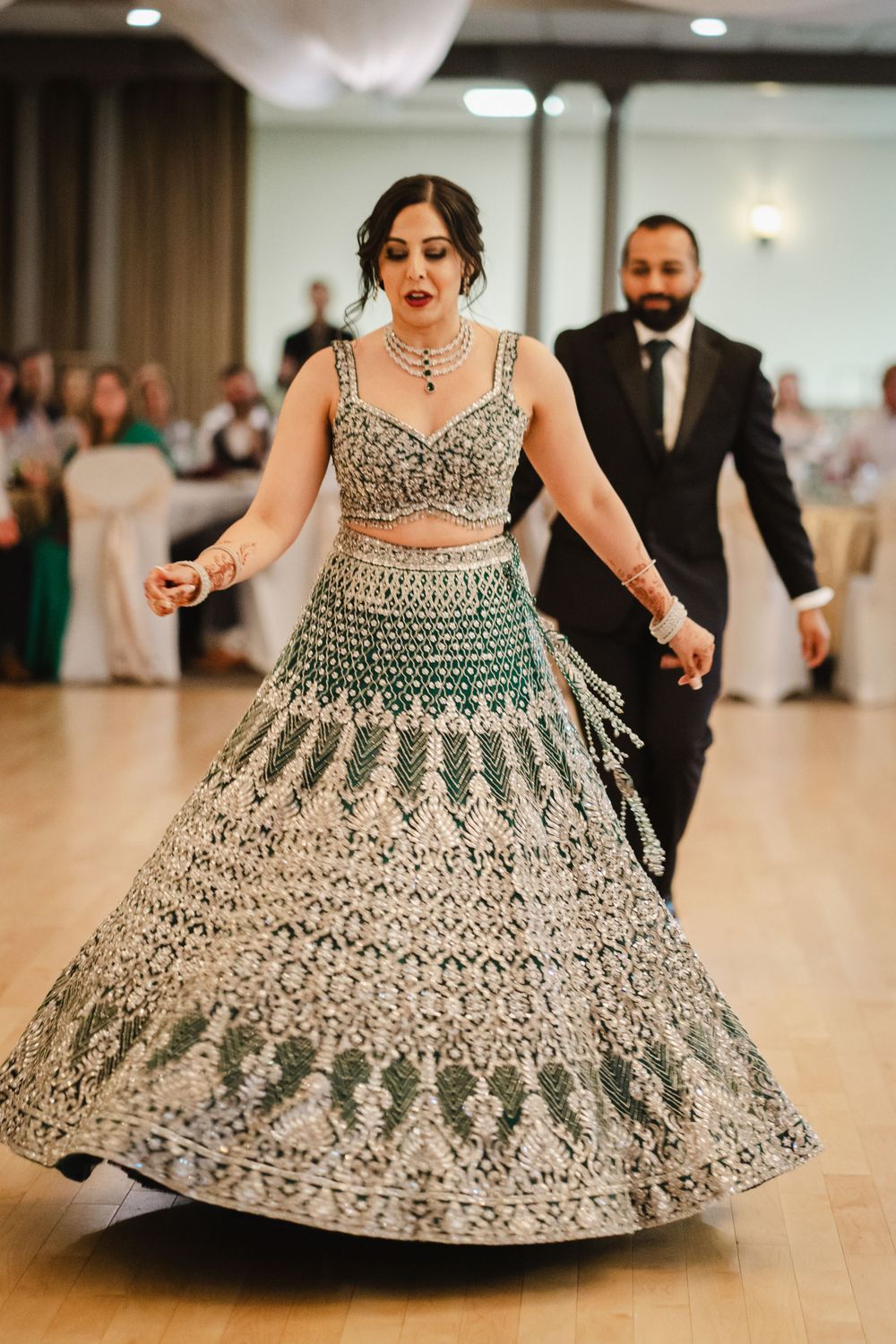 A dancer twirls in an intricately embroidered green and white lehenga on a wooden dance floor.