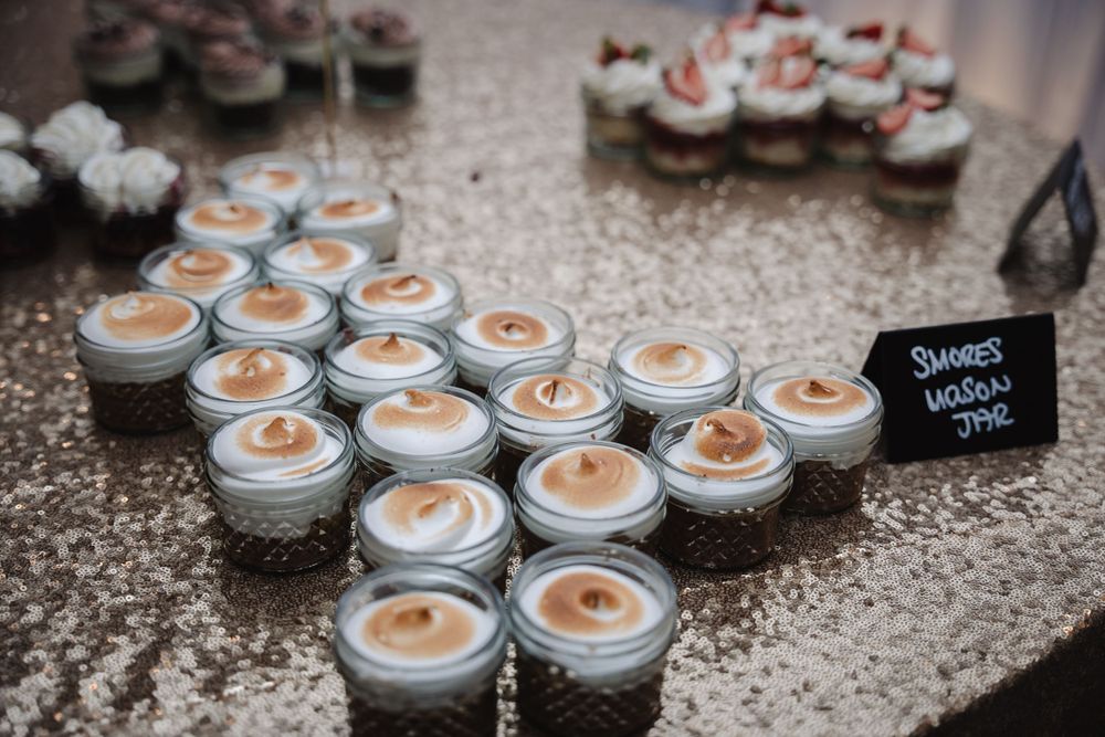 Rows of small jars with orange-tinted candles arranged on a sparkly surface at a wedding reception.