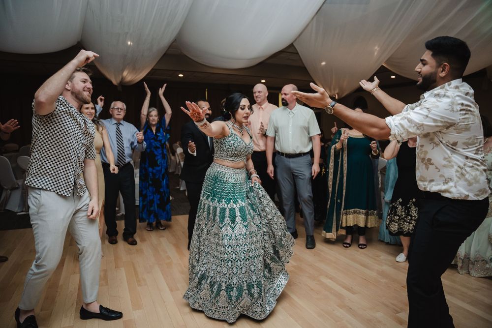 Wedding celebration with guests dancing in a circle around a person in an elaborate green lehenga.