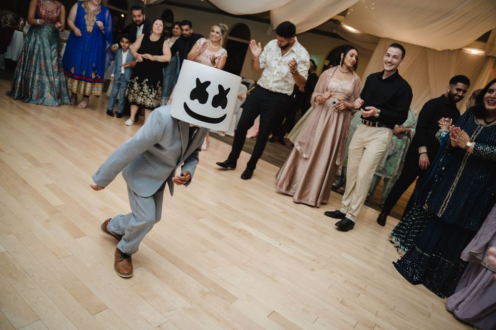 A performer in a Marshmello mask dances on the wooden floor during a wedding reception.