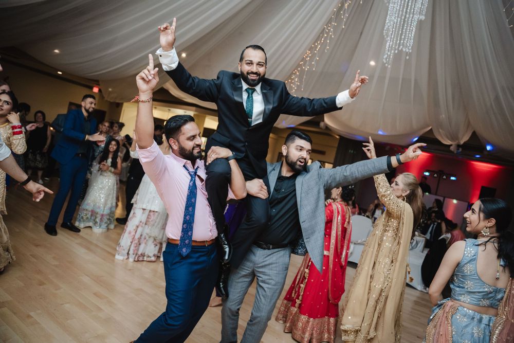 Joyful wedding guests lift someone up during festive dancing at a reception with draped fabric decor.