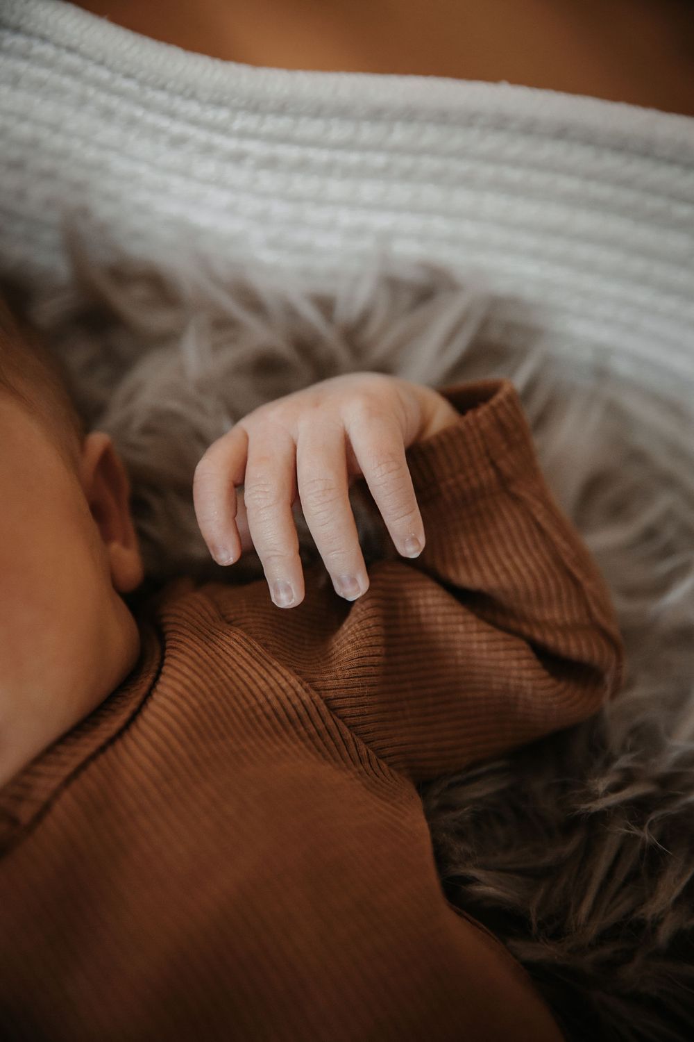 A small hand rests on brown textured fabric against white bedding.