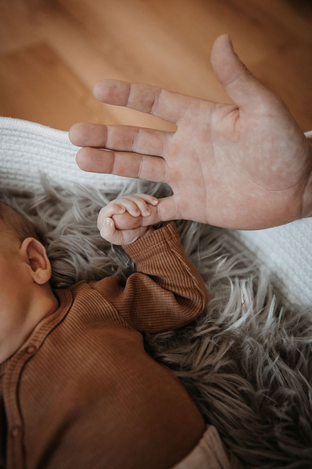 Close-up of tiny baby fingers grasping an adult hand against a soft gray blanket.