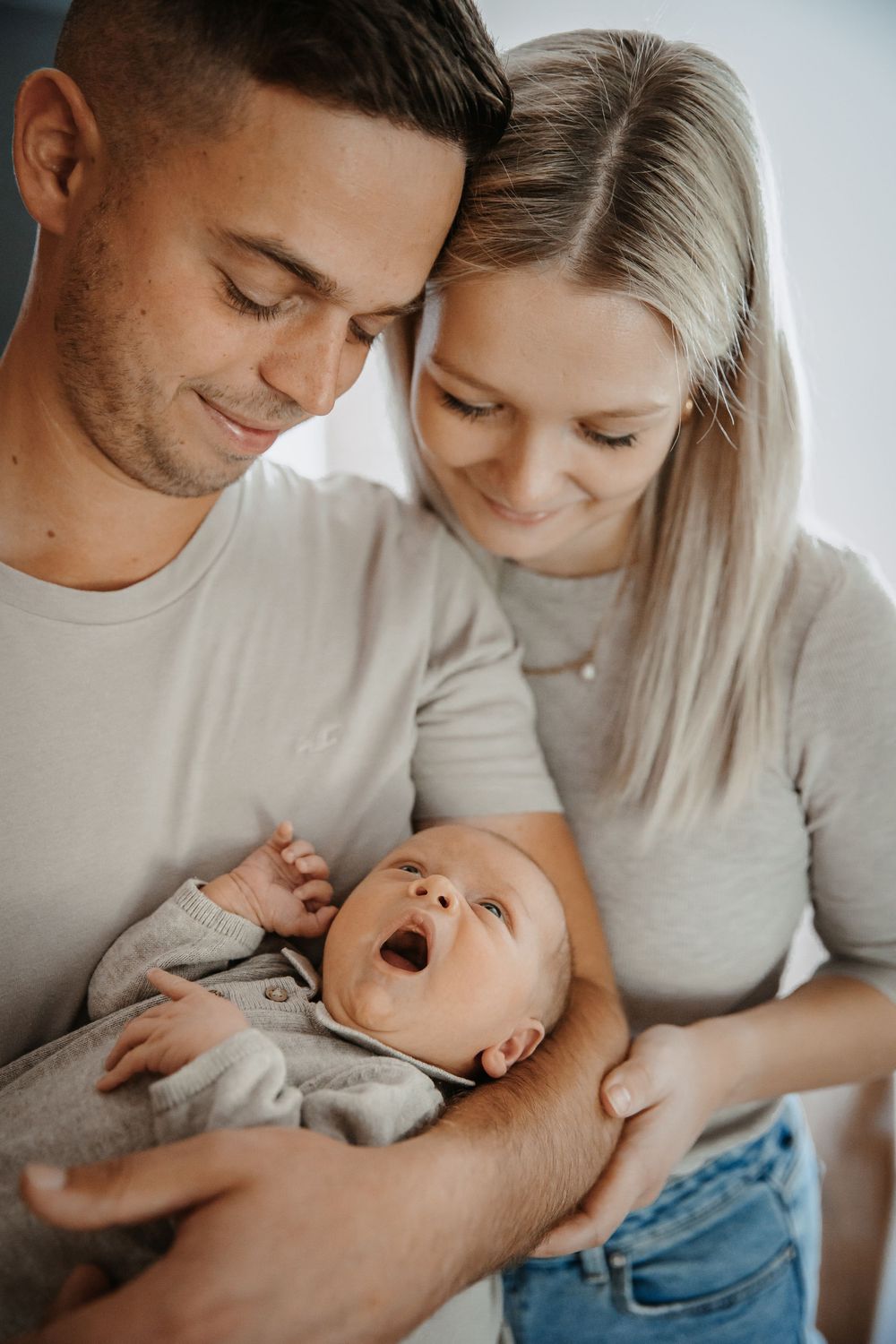 Intimate family moment with couple in white shirts cuddling their newborn baby.