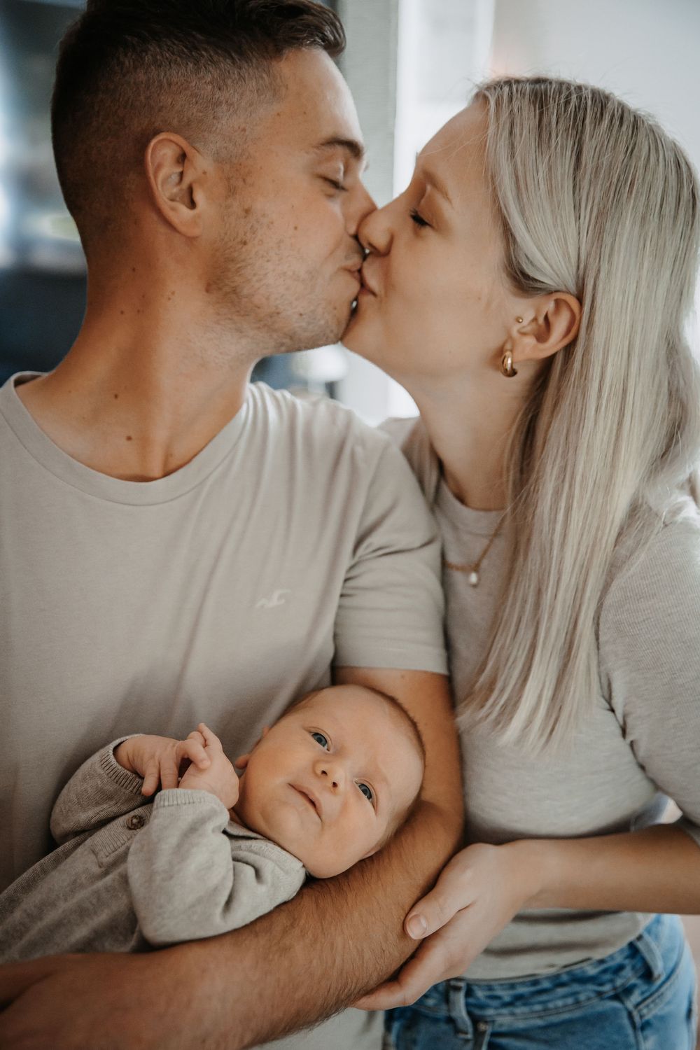 Tender family moment as couple shares affection while holding their newborn.