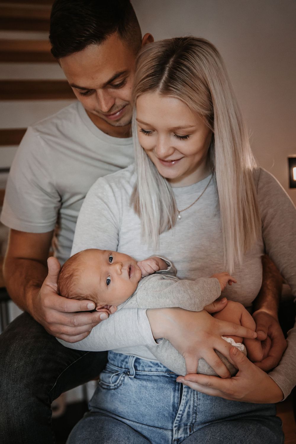 Couple in casual wear sharing tender moments with their newborn baby at home.