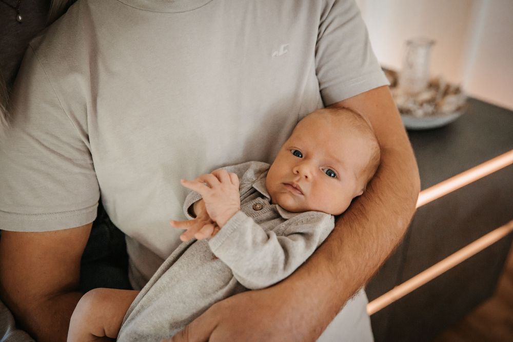 Parents in gray shirts tenderly holding and gazing at their newborn baby.