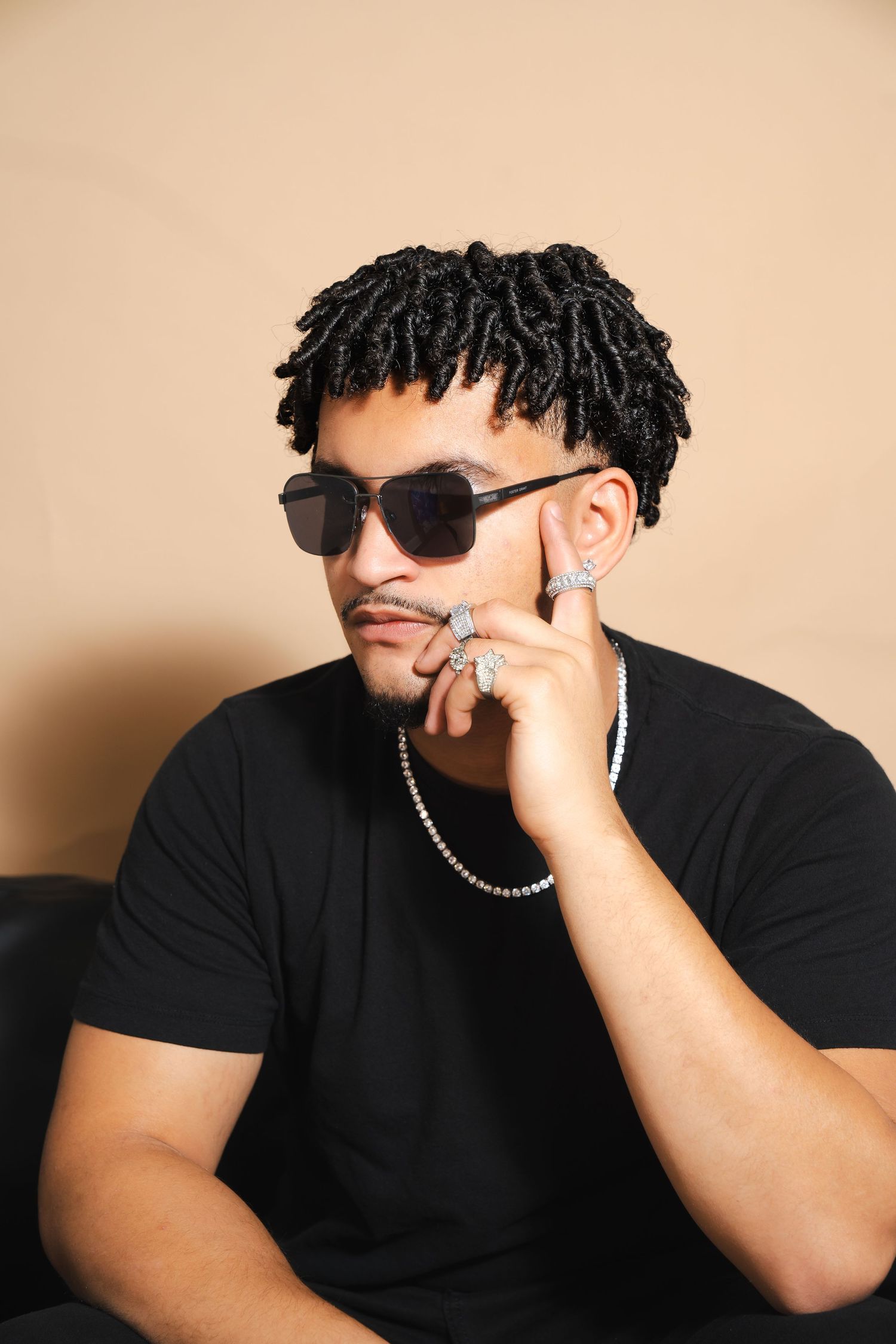 Studio portrait of person in black t-shirt wearing sunglasses with twisted hair and chain accessories.