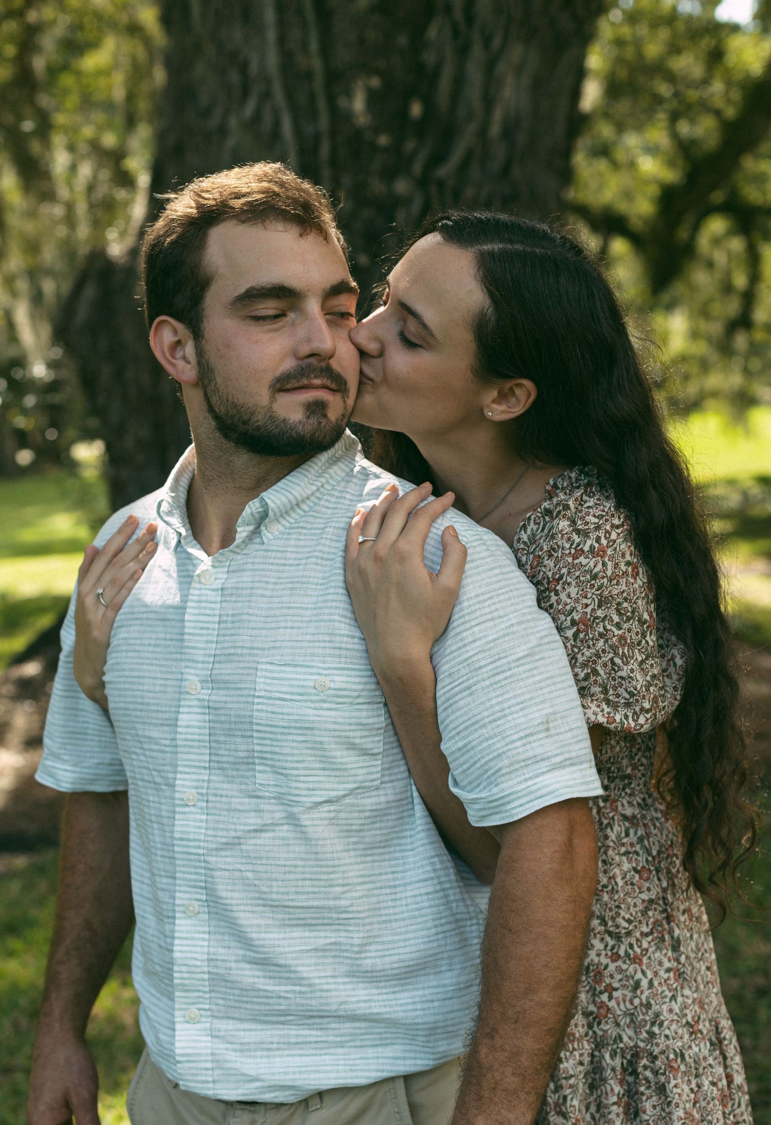 An intimate romantic moment captured between a couple in a sun-dappled garden setting.