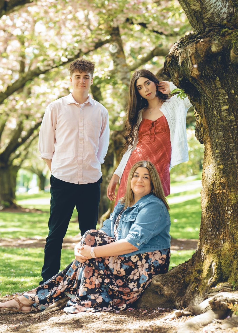 A group in casual spring attire poses together under a blooming tree in a sunny park setting.
