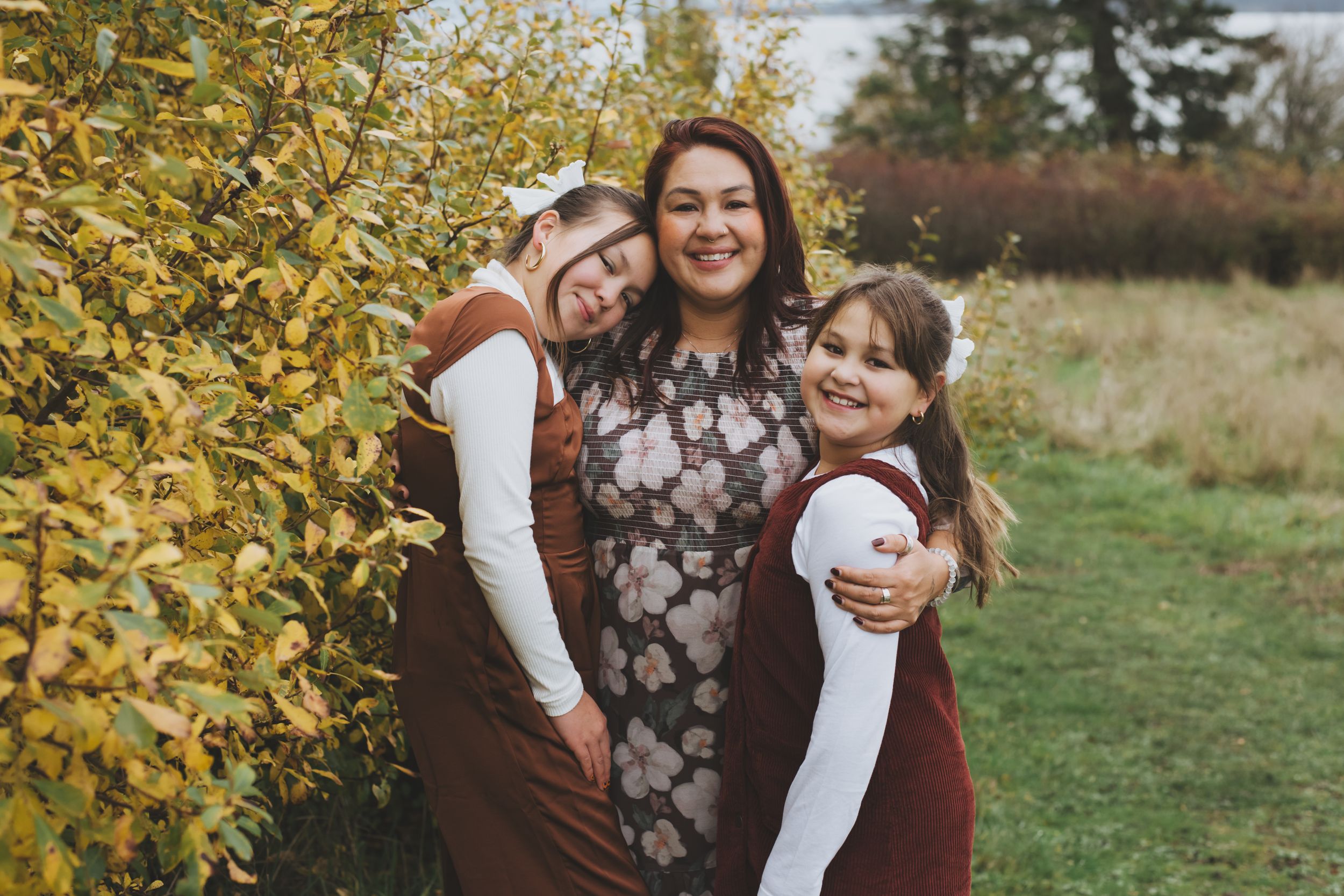 Mother embracing her two daughters with love, surrounded by vibrant autumn foliage.