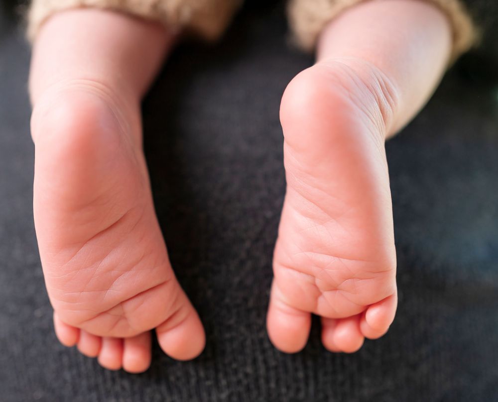 Close-up of tiny newborn baby feet resting on a dark gray surface, showing delicate toes and soft skin.