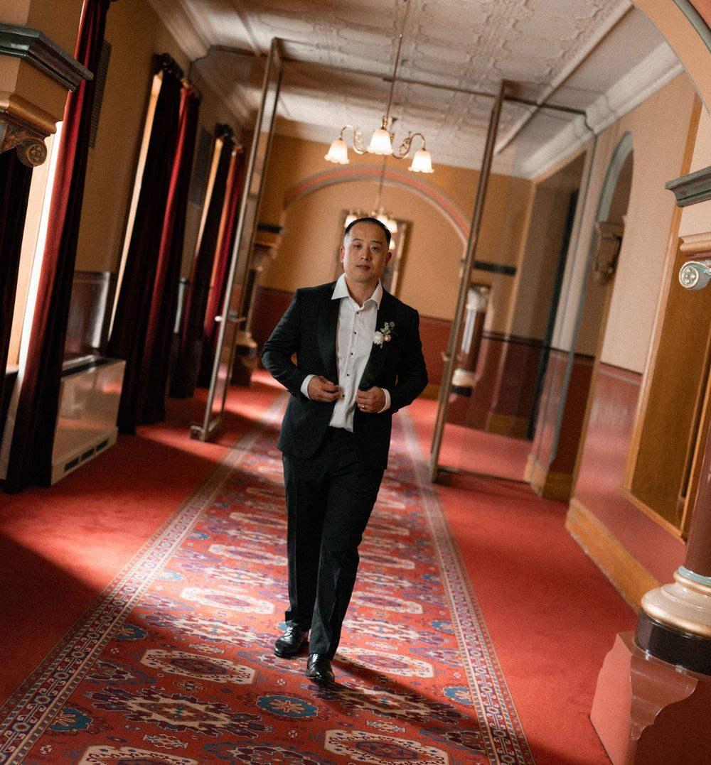 Person in formal attire walks down an ornate hotel hallway with red carpeting and elegant wall sconces.