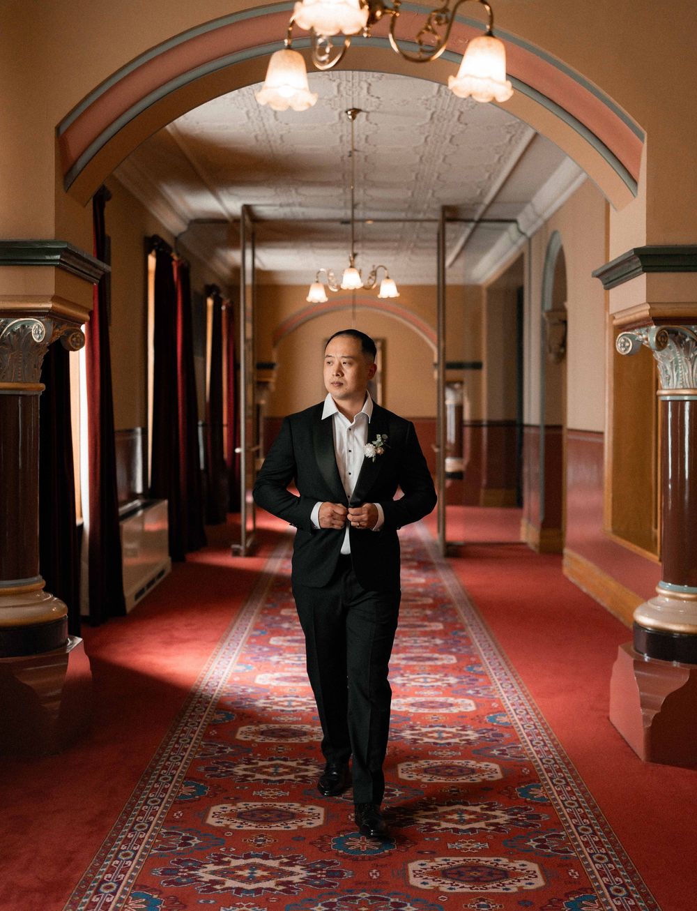 A person walks down an elegant hallway with ornate architectural details, red carpet and vintage light fixtures.