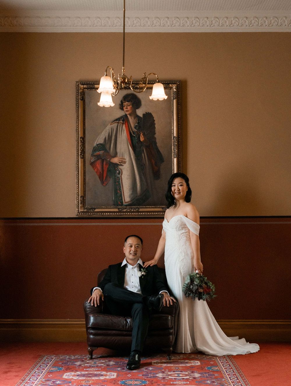 Wedding couple poses in an elegant indoor setting with vintage furniture and warm lighting.