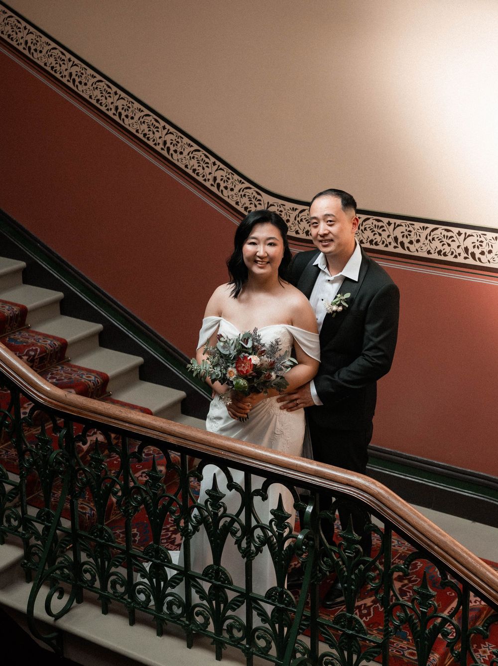 Newlyweds share a moment on an ornate staircase with decorative iron railings.