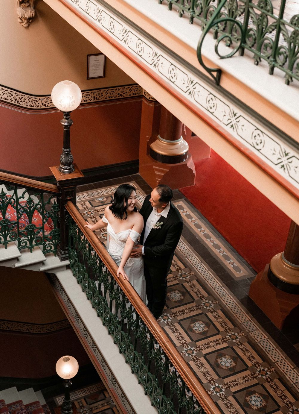 A staircase with ornate iron railings and decorative moldings features someone walking up the steps in formal attire.