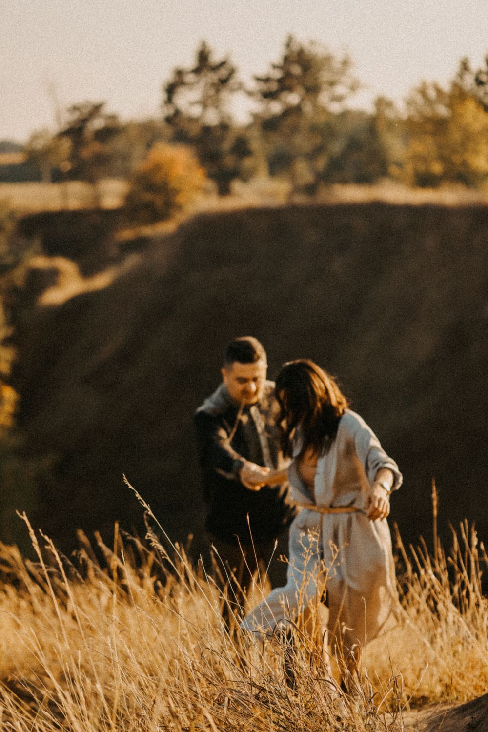 A couple walking together through golden grass at sunset in a natural setting.