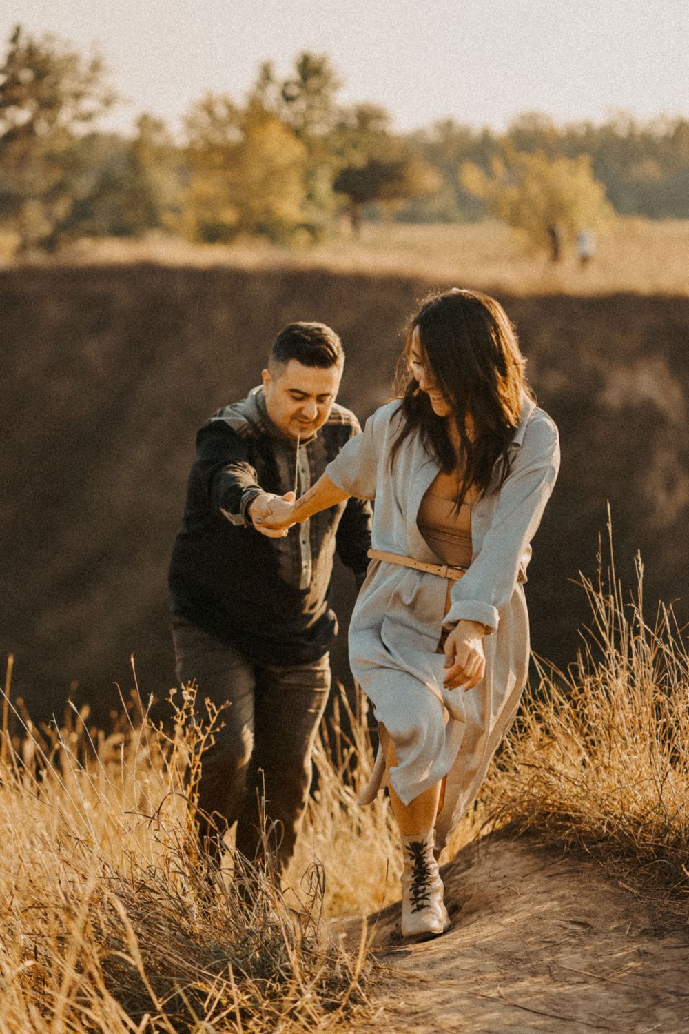 A couple walks together at sunset on a trail surrounded by golden grass and autumn trees.