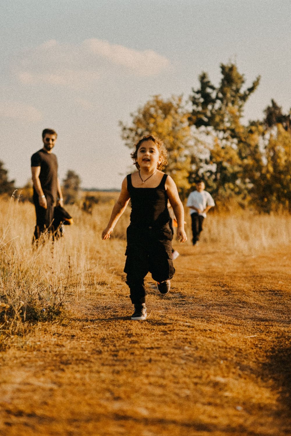 A group of people walking on a golden dirt path through tall grass during warm sunset lighting.