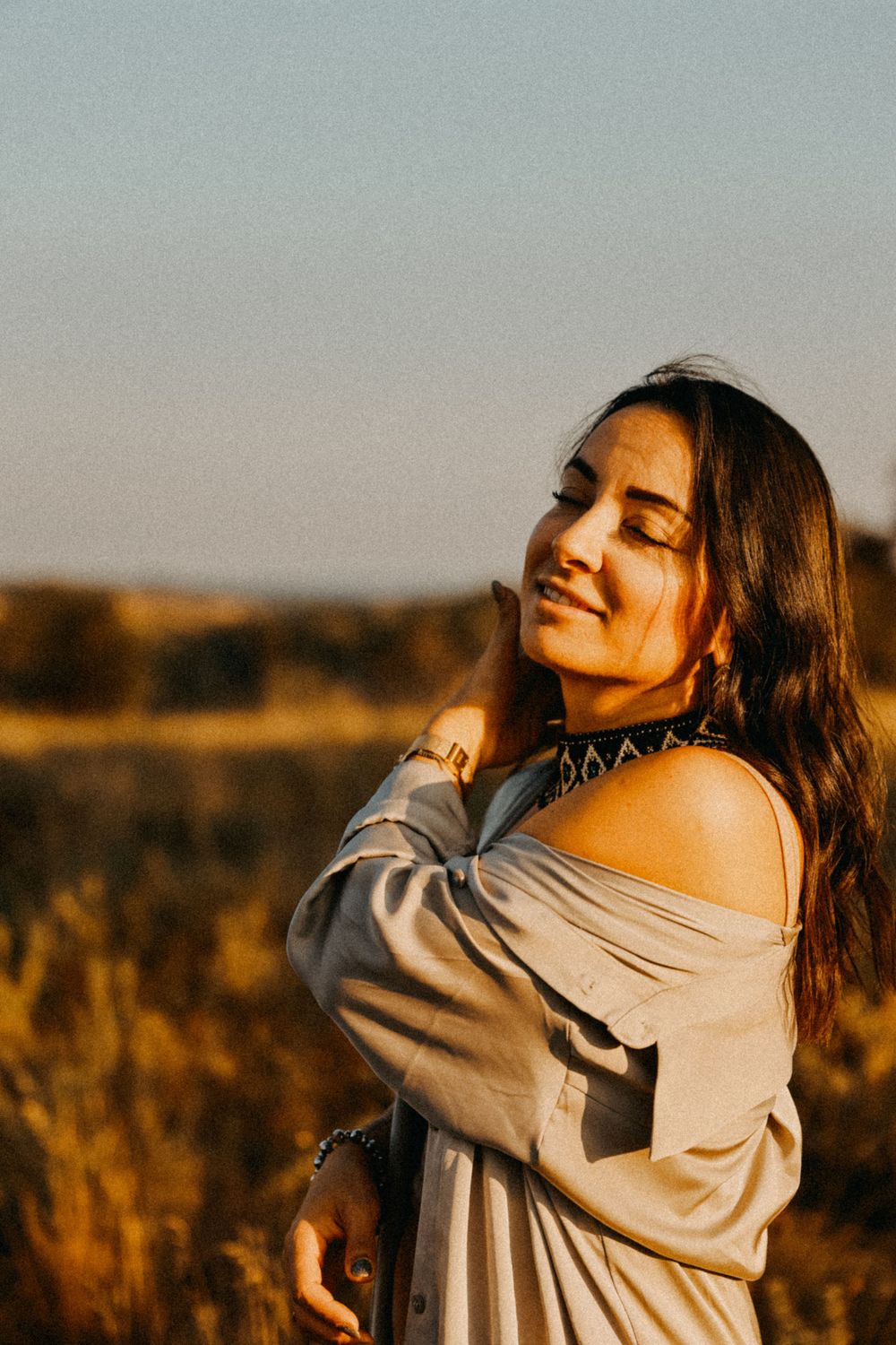 Portrait of someone in an off-shoulder beige dress against golden hour lighting in a field of tall grass.