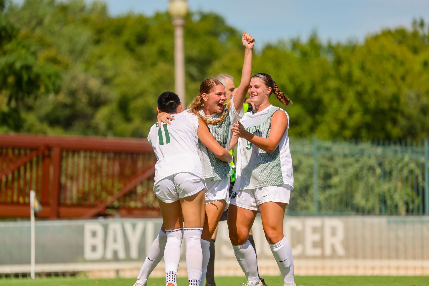 Female soccer players celebrating a goal on a Baylor University soccer field.