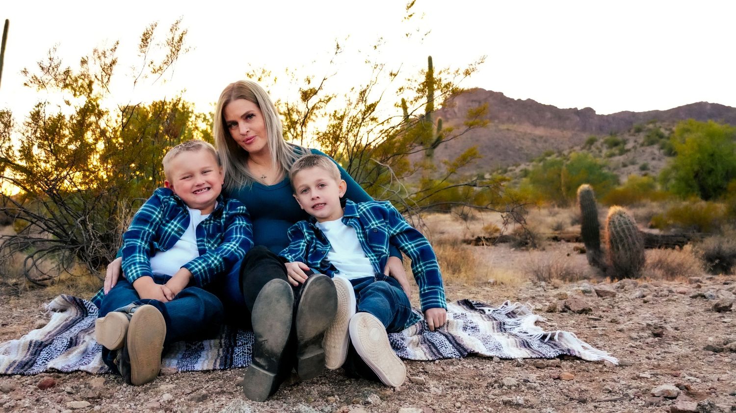 A photograph of a mom and her two sons sitting on a blanket with the sunset behind them for a family photography session in Queen Creek, AZ.