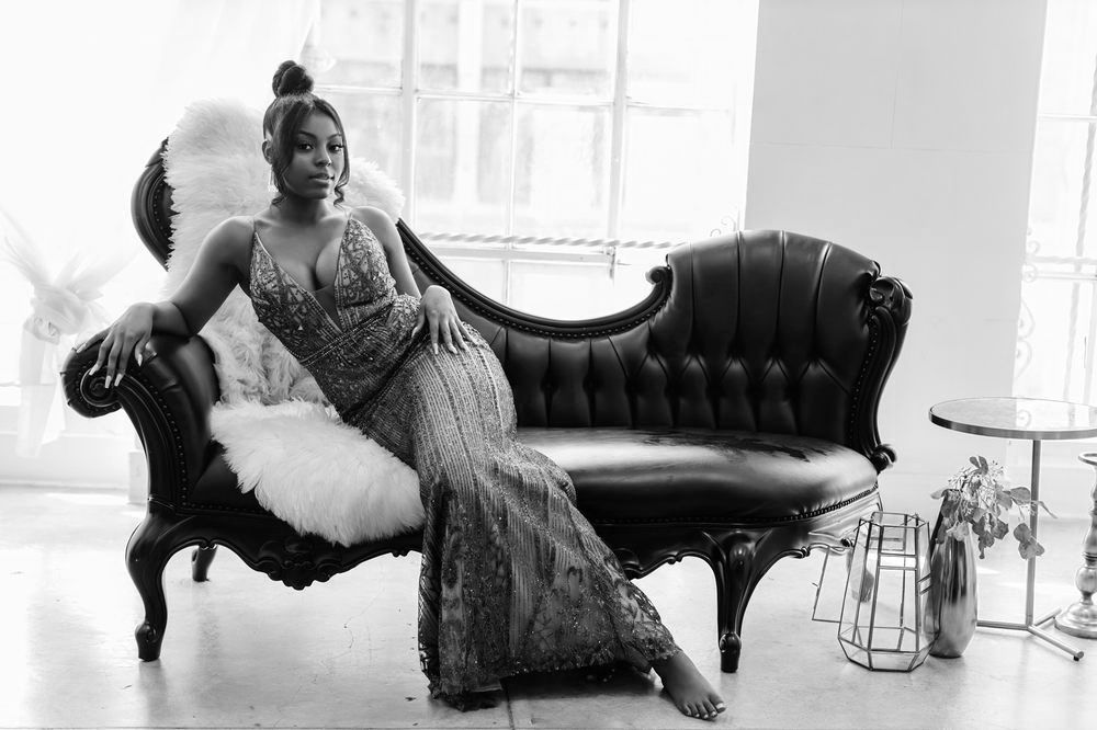 Person in glamorous sequined dress reclining on vintage black chaise lounge.
