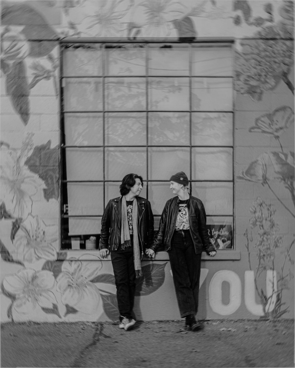A black and white artistic photo of two figures in suits standing against a wall with floral decorative elements.