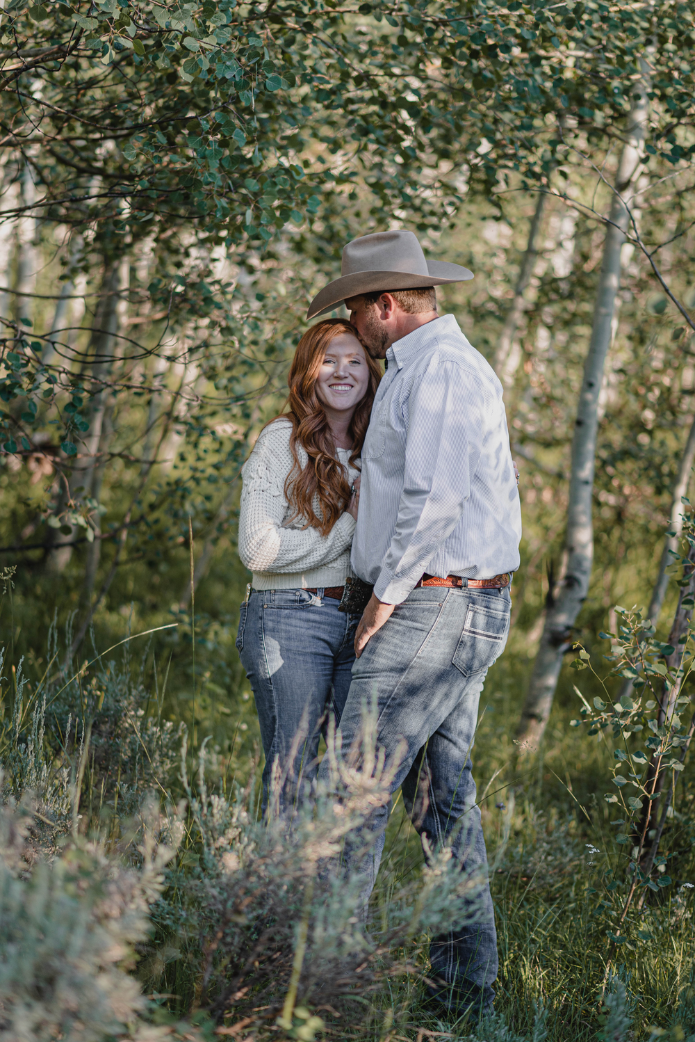 A couple share an intimate moment together among aspen trees in a rustic outdoor setting.