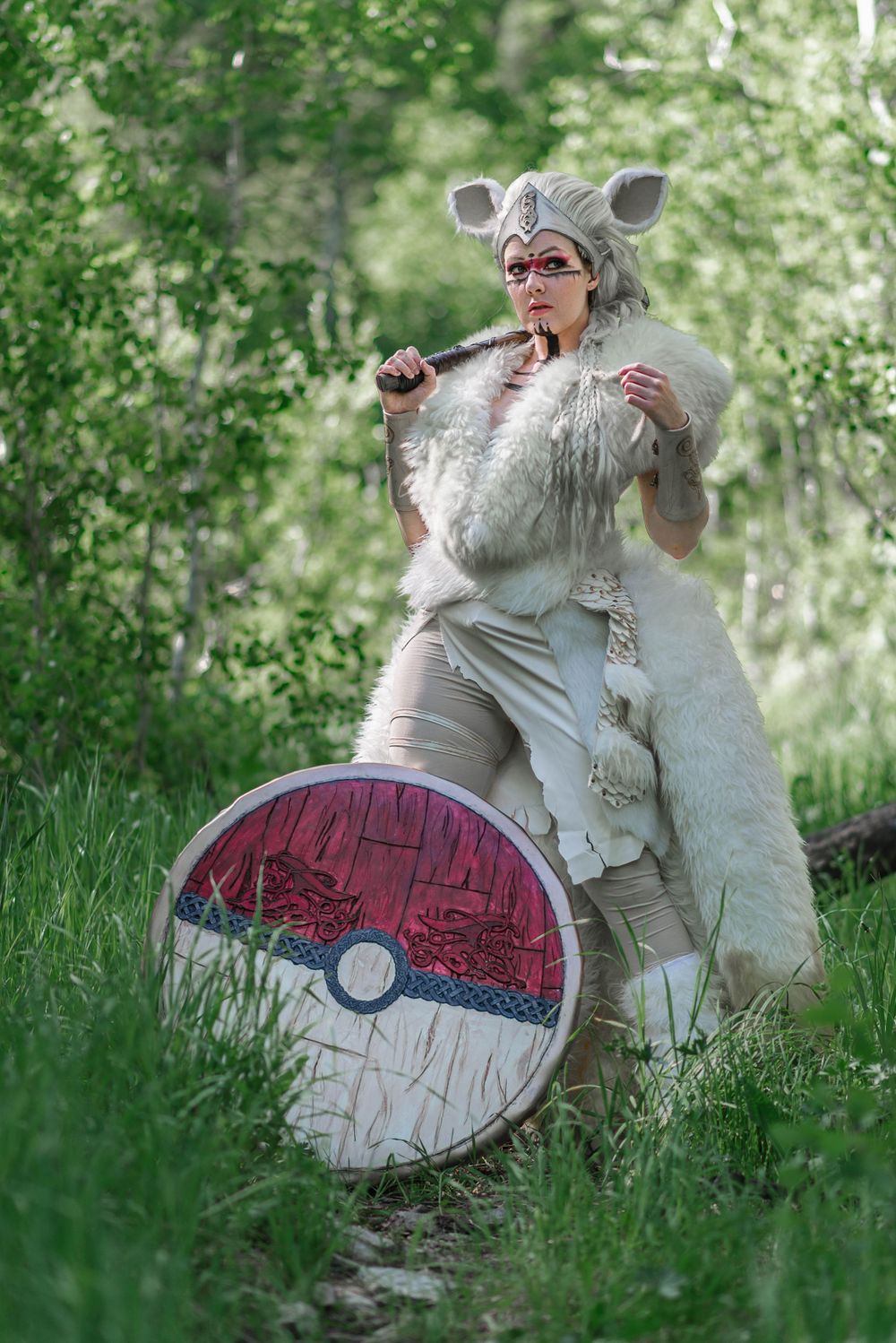 Pokemon-inspired cosplay with furry ears and Pokeball shield in forest setting.