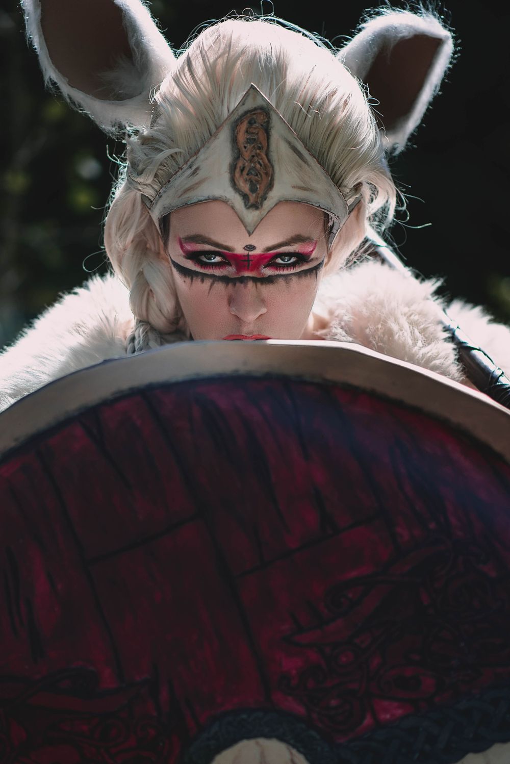 Fantasy warrior cosplay with white fox ears and dramatic makeup behind shield.