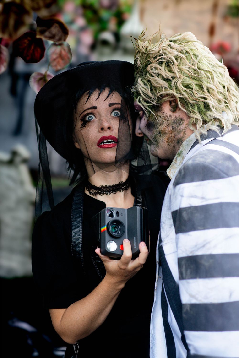 A gothic-styled Halloween scene with two people in costumes holding a vintage camera.