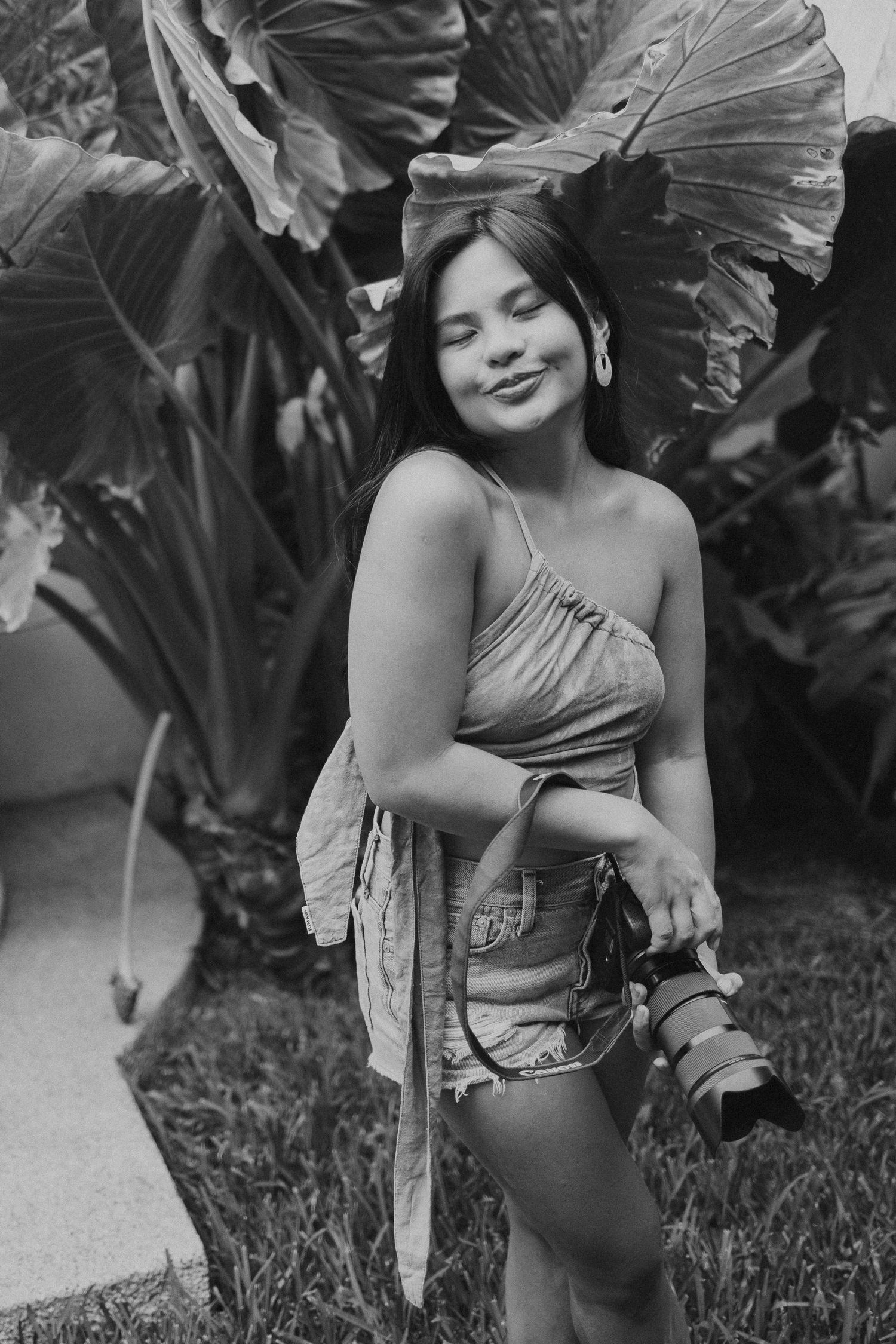 Black and white portrait of photographer with camera among large tropical leaves.
